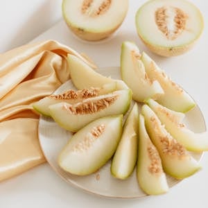 Delicious honeydew melon slices on a plate with beige fabric for a fresh and elegant food presentation.